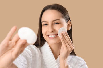 Poster - Young woman in bathrobe with cotton pads removing makeup on brown background, closeup