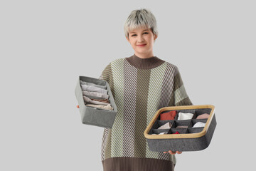 Beautiful young woman holding organizers with clothes on grey background