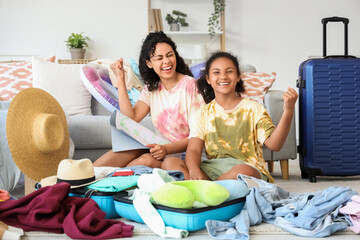 Canvas Print - Happy young African-American woman and her daughter packing suitcase and showing yes gesture at home. Travel concept