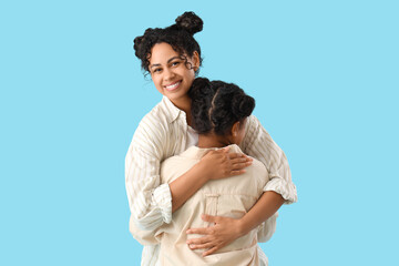 Poster - Happy young African-American woman with her daughter hugging on blue background