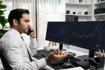 Trader businessman calling to consultant or partner with two stock exchange investment, compare data analysis to invest high profit value dynamic financial technology stock market at office. Surmise.