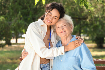 Wall Mural - Young African-American female medical worker hugging with elderly woman outdoors