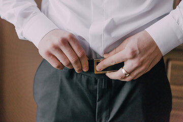 Wall Mural - A man fastens a black leather belt around his waist. Man's hands close-up.