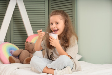 Poster - Cute little girl sitting on bed and eating yogurt in room