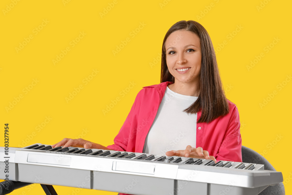 Young woman playing synthesizer on yellow background