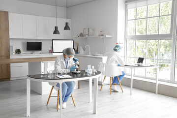 Wall Mural - Female scientist looking through microscope at table in laboratory