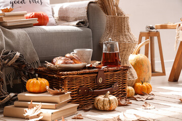 Wall Mural - Autumn composition with teapot, cup of hot beverage, tasty buns and pumpkins on wicker basket in living room