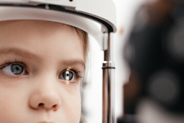 A little girl undergoes an eye test by a professional optometrist using modern diagnostic equipment in ophthalmology clinic. Beautiful female eye with yellow laser ray. Vision correction. Macro shot