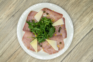 Overhead view of Italian appetizer with raw tuna with slices of parmesan cheese, arugula, and capers arranged on a plate