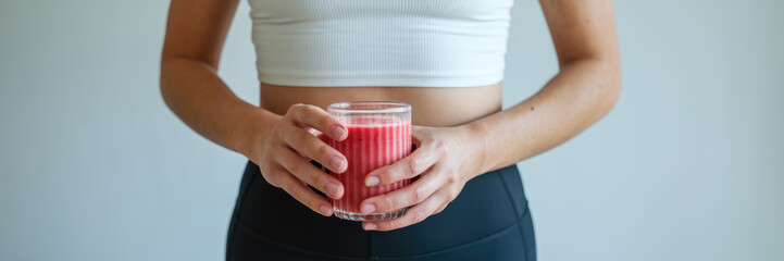 A woman is holding a glass of red juice. She is wearing a white tank top