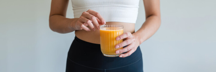 A woman is holding a glass of orange juice. She is wearing a white tank top