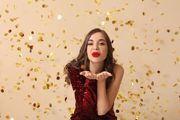 Sticker - Young woman blowing kiss and falling confetti on beige background. New Year celebration