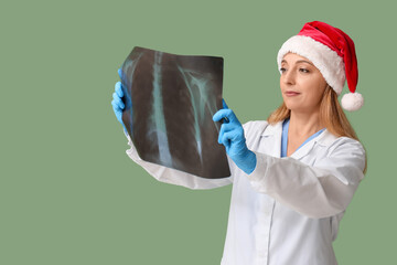 Canvas Print - Mature female doctor in Santa hat with x-ray image on green background