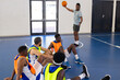© Wavebreak Media - Basketball coach holding ball and instructing team players sitting on court