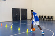 © Wavebreak Media - Dribbling basketball, athlete practicing agility drills with cones in gymnasium, copy space