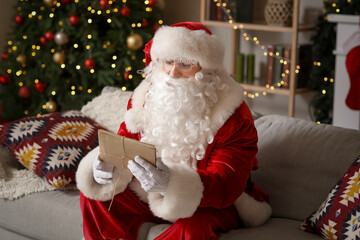 Poster - Santa Claus with letters sitting on sofa at home