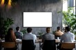 © Downloads - A group of businesspeople sitting around a conference table in a modern well lit boardroom looking at a large blank TV screen displayed on the wall