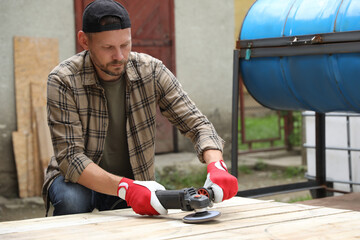 Poster - Man polishing wooden planks with angle grinder outdoors