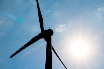 Photo of wind turbine silhouette against the sun and a blue sky.