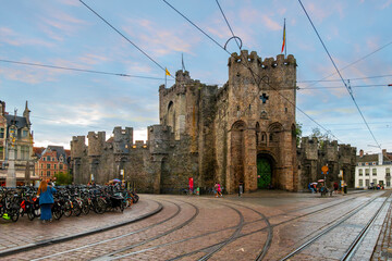 Early evening twilight view of the medieval Gravensteen Castle built in 1180 as it runs past public transport tram tracks in the historic old town of Ghent, Belgium.