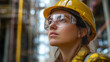 © Andres Mejia - Female engineer wearing safety glasses and hard hat looking up at refinery
