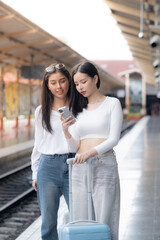 Two happy female walk around sign seeing siting at the station while waiting for a train.