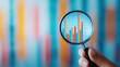 © Wonderful Studio - Hand holding magnifying glass over financial growth graph with colorful bars.