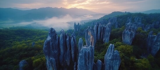 Wall Mural - aerial view of a misty forest with tall, sharp rock formations rising up from the trees at sunrise.