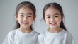 © Snowstudio - close-up of two asian girls children twins in white t-shirts, smiling at the camera against light gray background