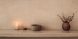 © JuanM - A tranquil shelf display with candles, a clay bowl, and a vase of dried flowers against a warm, neutral background
