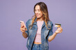 © ViDi Studio - Young woman wear denim jacket violet top casual clothes using mobile cell phone hold credit bank card shopping online order delivery booking tour isolated on plain purple background Lifestyle concept