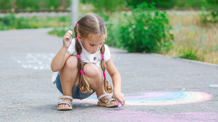 Cute girl drawing colored chalk on the asphalt on summer sunny day. Creative development of children. Sidewalk chalk games for kids