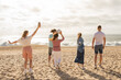 © Prostock-studio - A group of five friends gathers on a sandy beach, having fun and laughing while tossing a volleyball under the sun. The ocean waves crash gently in the background.