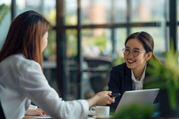 Female Asian translator works with smiling businesswoman in corporate setting. Happy woman, attractive man collaborate at office desk. Smiling faces positive attitude, pro teamwork. Corporate