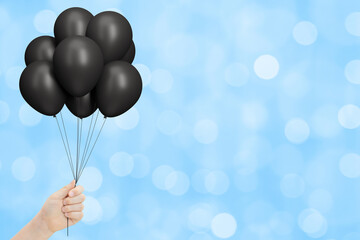 Aufkleber - Female hand holds bunch of black balloons on blurred blue background. Empty space for text