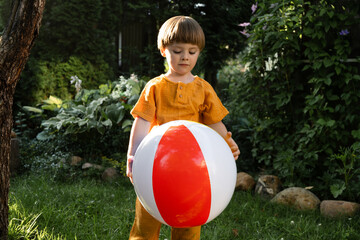 Small boy playing with beach ball on lawn in summer.