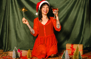 A beautiful happy young woman in a Santa hat holds a cocktail and a sparkler