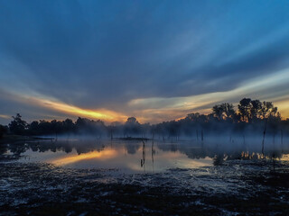 Sky colors at sunrise with sun rays in the morning fog over the water