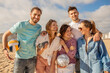 © Prostock-studio - A group of five friends is happily spending a sunny day at the beach, enjoying activities like beach volleyball and music, creating joyful memories by the ocean.