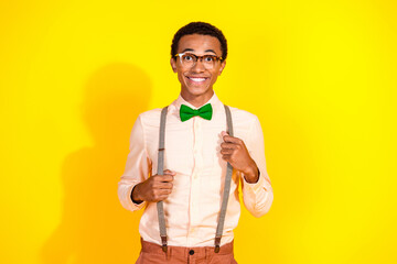 Poster - Photo of elegant young man arms hold suspenders wear shirt bow tie isolated on yellow color background