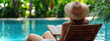 © oksa_studio - Woman relaxing with book near luxury resort pool