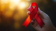 © anantachat - Close-up of a hand holding a red ribbon symbolizing support for World AIDS Day with a blurred background highlighting the significance Large space for text in center Stock Photo with copy space