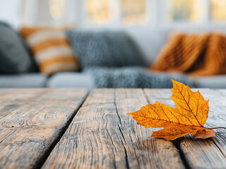 Poster - Single yellow maple leaf lying on a wooden table with a sofa in the background