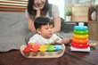 © Prathankarnpap - Adorable toddler boy playing with colorful toys while mother lovingly watches. Childhood and nurturing care concept