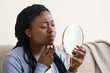 © Prostock-studio - Problem Skin Concept. Black Woman Looking In Round Mirror and Touching Her Face, Worry About Pimple, Closeup