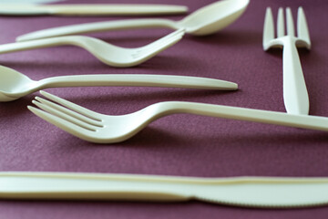 White plastic cutlery forks and spoons on colorful dark pink violet background, eco friendly