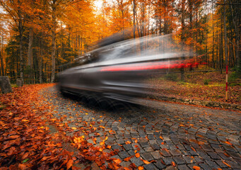 Wall Mural - blurred car on winding cobblestone road in forest in autumn