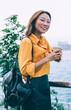 © BullRun - Half length portrait of cheerful Asian tourist with coffee to go in hand standing near river and metropolis landscape on background smiling and enjoying free time for coffee to go in Hong Kong