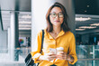 © BullRun - Half length portrait of attractive female blogger in optical spectacles for provide eyes protection smiling at camera during coffee break for networking with cellphone gadget, millennial person