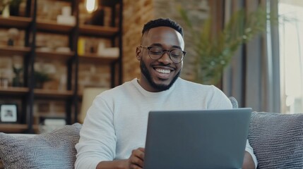 Poster - A man is sitting on a couch and smiling while using a laptop